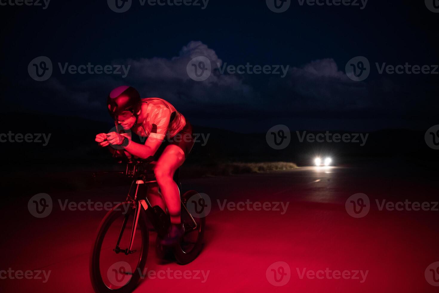 A triathlete rides his bike in the darkness of night, pushing himself to prepare for a marathon. The contrast between the darkness and the light of his bike creates a sense of drama and highlights the photo