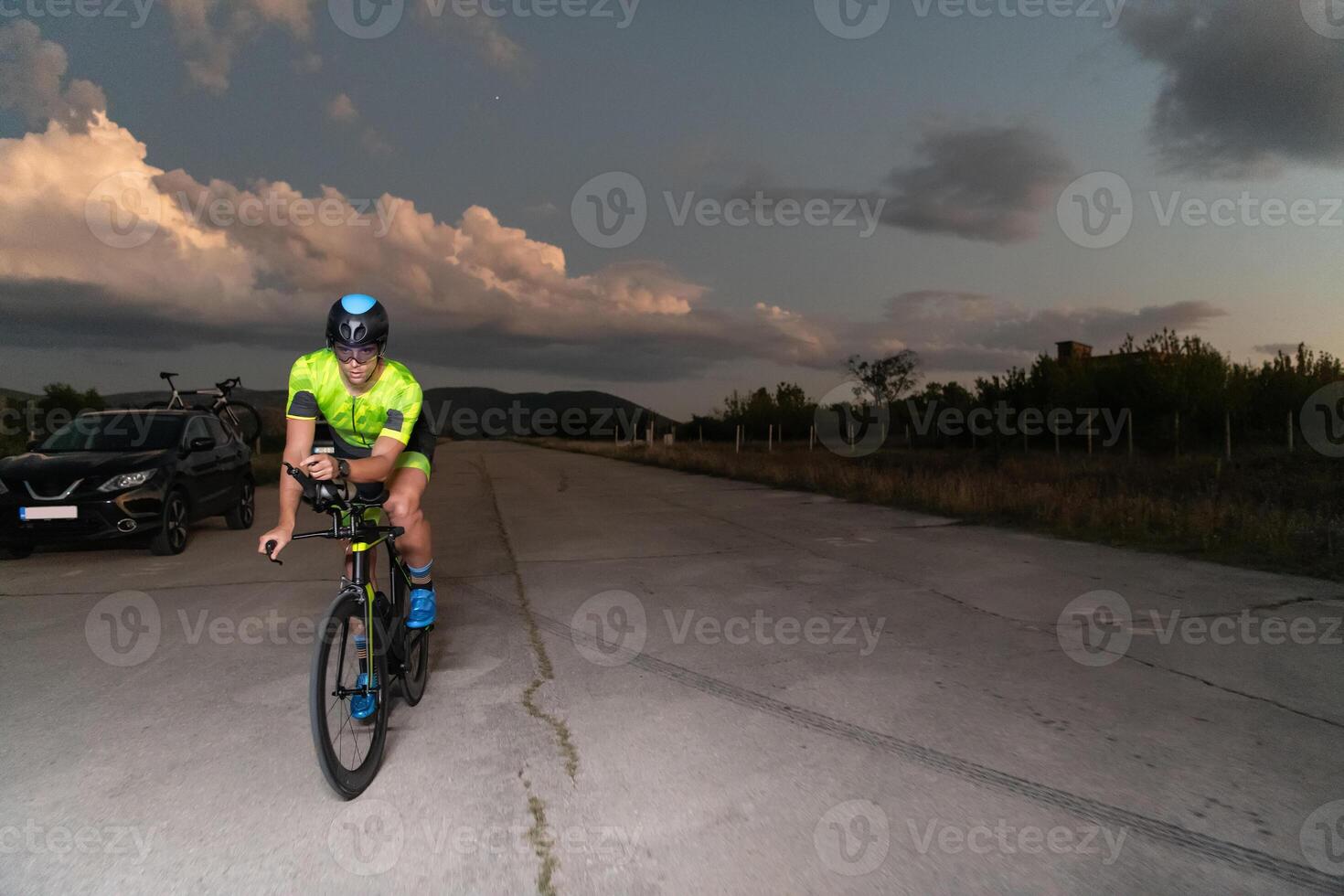 A triathlete rides his bike in the darkness of night, pushing himself to prepare for a marathon. The contrast between the darkness and the light of his bike creates a sense of drama and highlights the photo