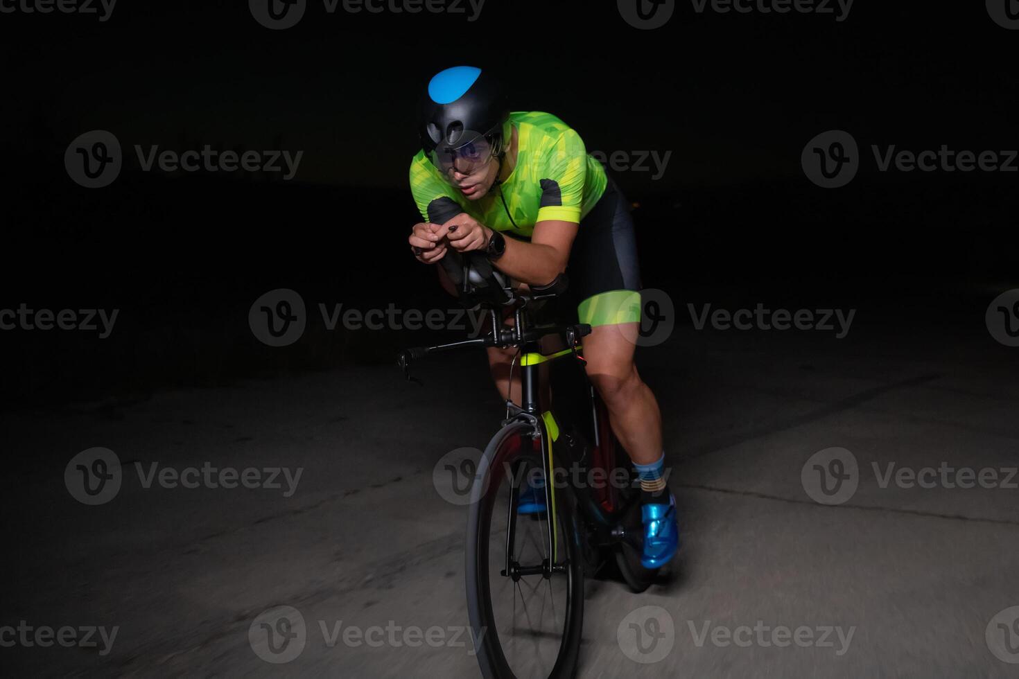 A triathlete rides his bike in the darkness of night, pushing himself to prepare for a marathon. The contrast between the darkness and the light of his bike creates a sense of drama and highlights the photo