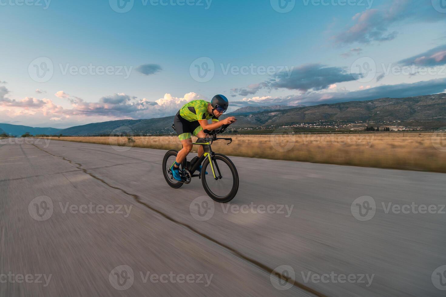 Triathlete riding his bicycle during sunset, preparing for a marathon. The warm colors of the sky provide a beautiful backdrop for his determined and focused effort. photo