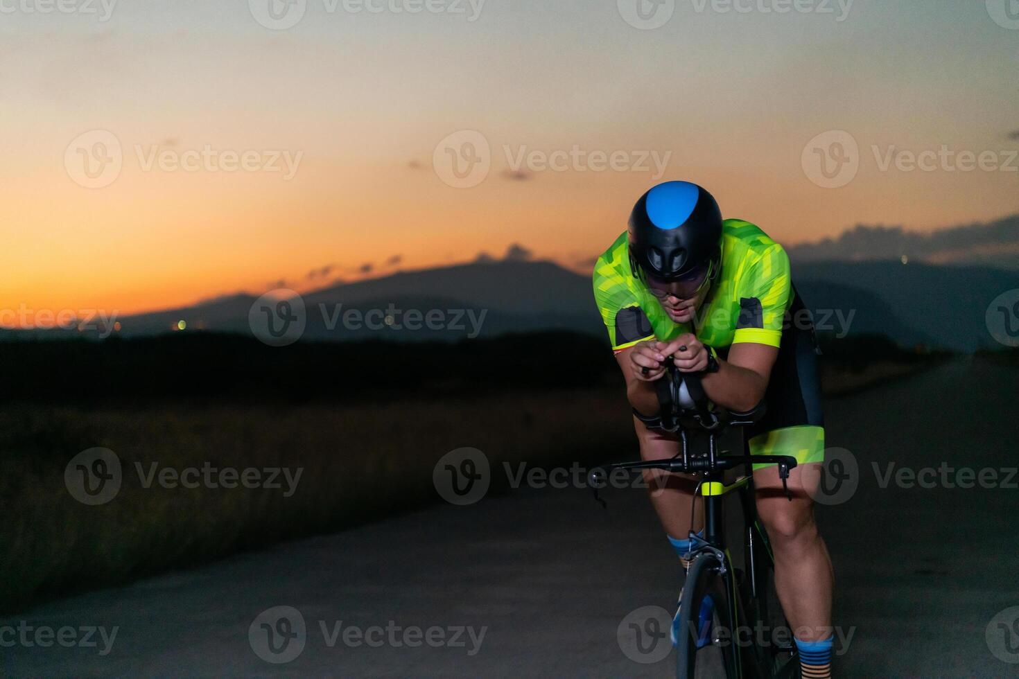 A triathlete rides his bike in the darkness of night, pushing himself to prepare for a marathon. The contrast between the darkness and the light of his bike creates a sense of drama and highlights the photo