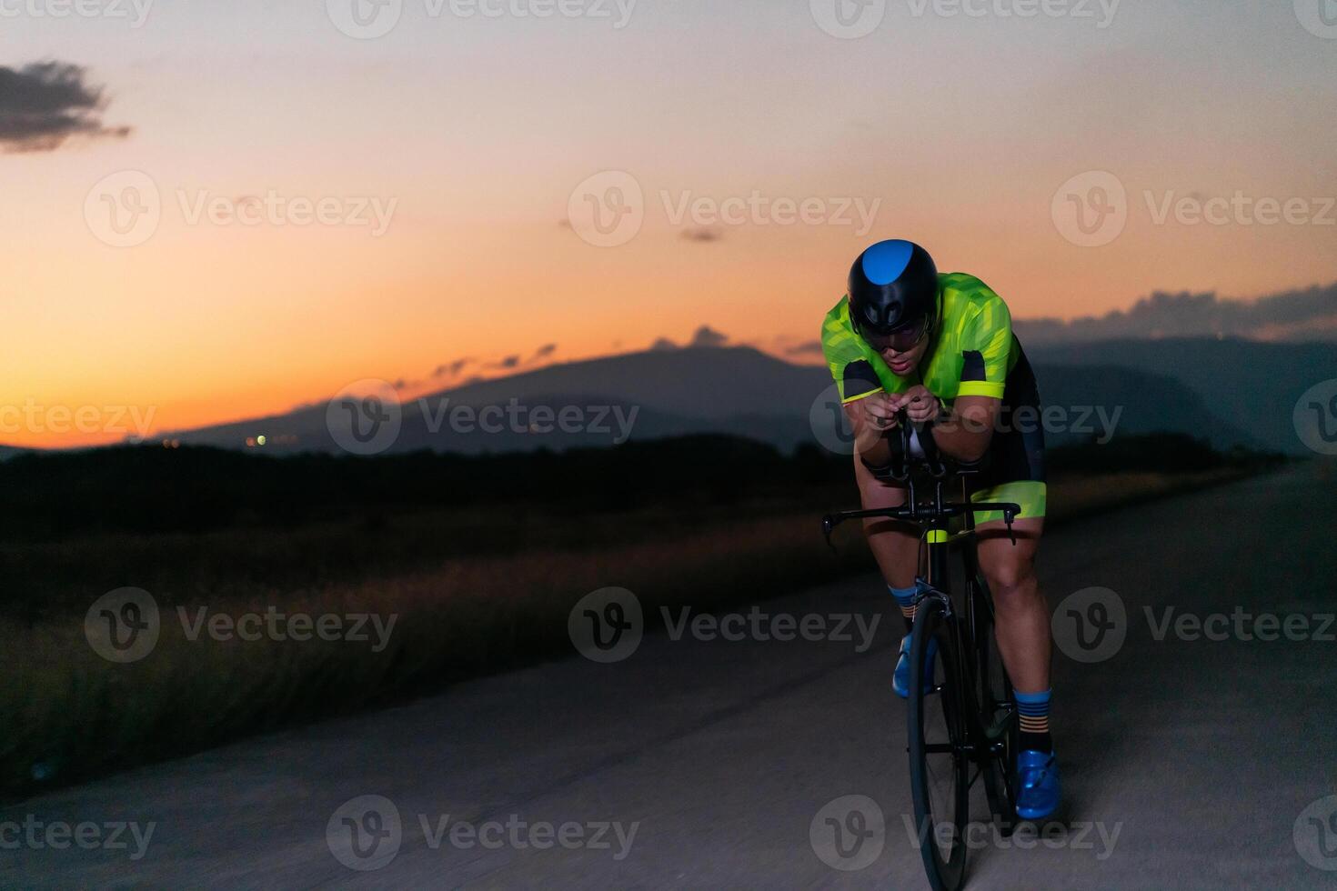A triathlete rides his bike in the darkness of night, pushing himself to prepare for a marathon. The contrast between the darkness and the light of his bike creates a sense of drama and highlights the photo