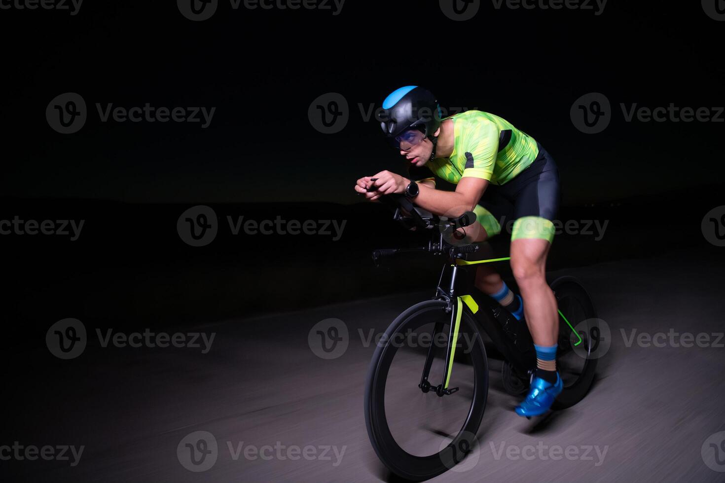 A triathlete rides his bike in the darkness of night, pushing himself to prepare for a marathon. The contrast between the darkness and the light of his bike creates a sense of drama and highlights the photo