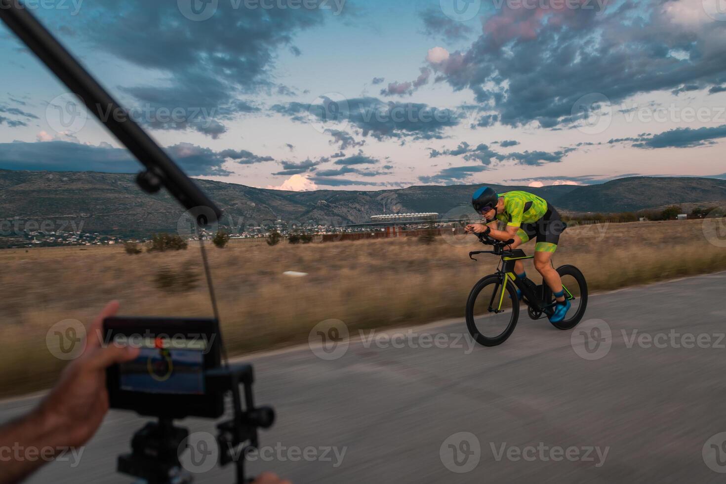 A videographer recording a triathlete riding his bike preparing for an upcoming marathon.Athlete's physical endurance and the dedication required to succeed in the sport. photo