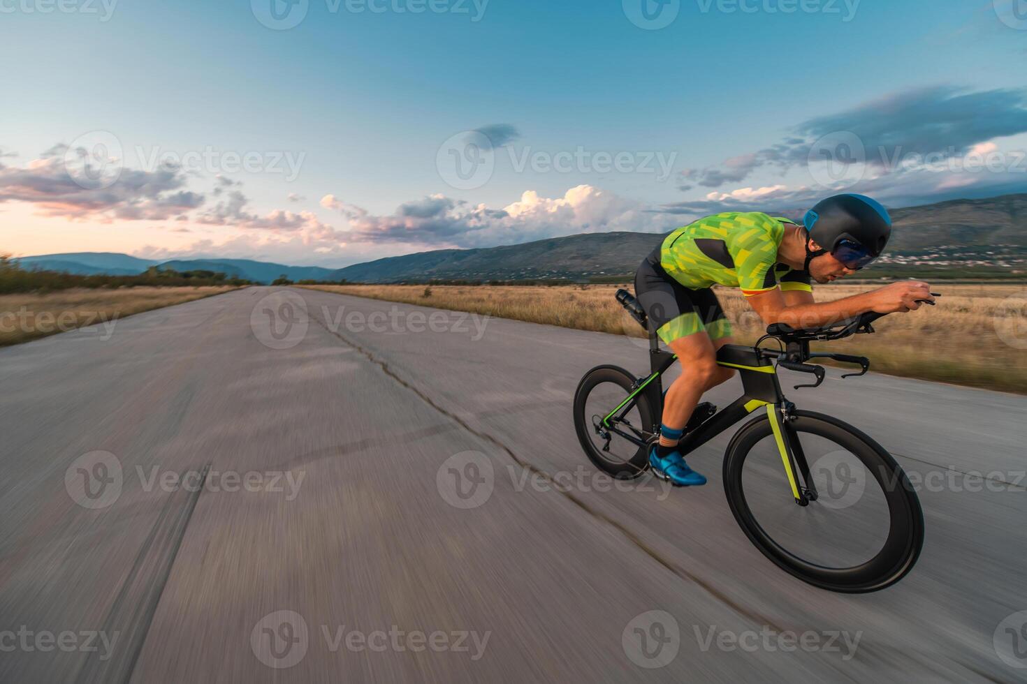 Triathlete riding his bicycle during sunset, preparing for a marathon. The warm colors of the sky provide a beautiful backdrop for his determined and focused effort. photo