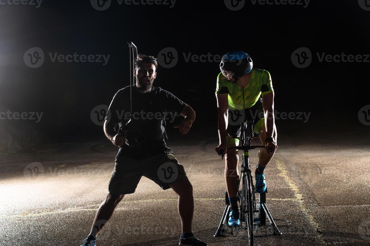Behind the scenes. Professional videographer on a night shoot with a triathlete riding a bicycle for recording purposes photo