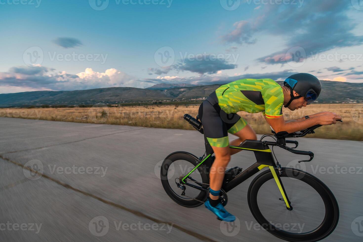 Triathlete riding his bicycle during sunset, preparing for a marathon. The warm colors of the sky provide a beautiful backdrop for his determined and focused effort. photo