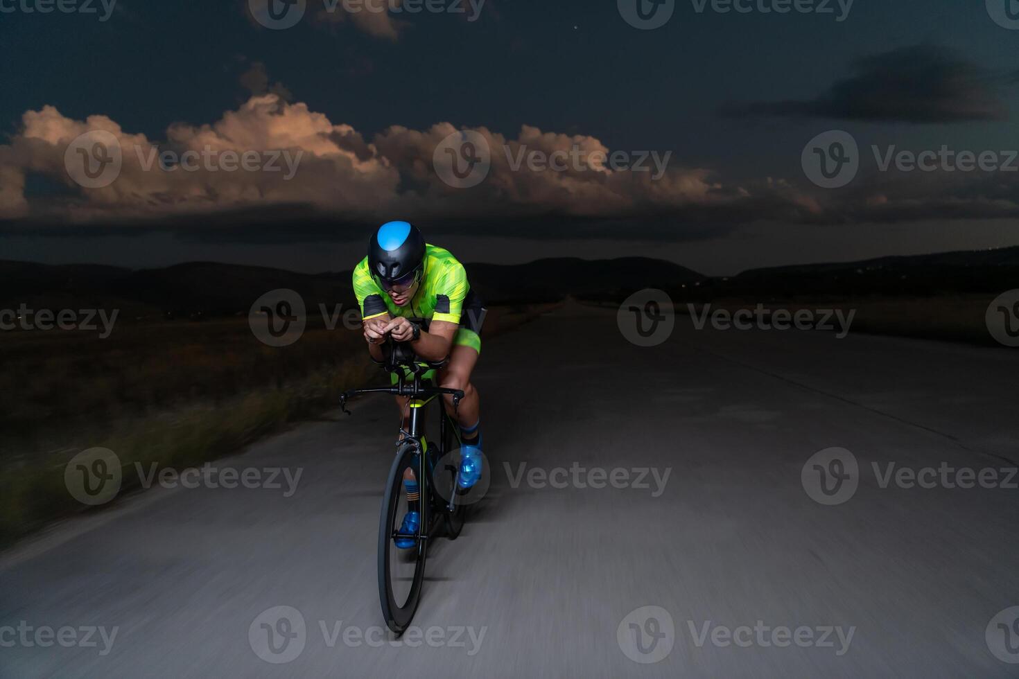 A triathlete rides his bike in the darkness of night, pushing himself to prepare for a marathon. The contrast between the darkness and the light of his bike creates a sense of drama and highlights the photo