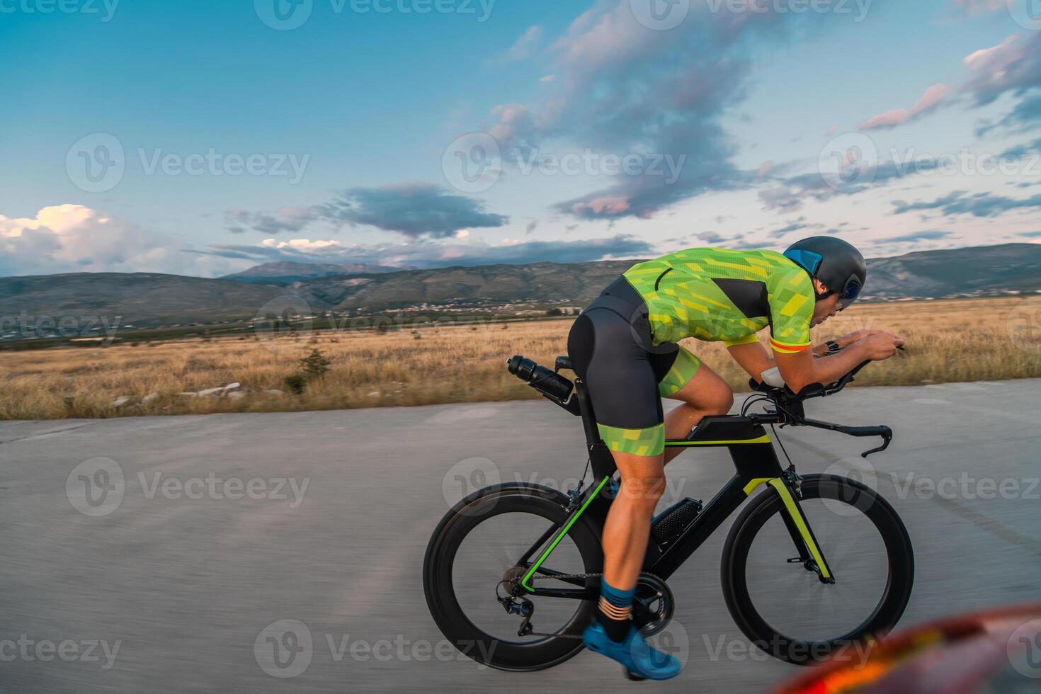 Triathlete riding his bicycle during sunset, preparing for a marathon. The warm colors of the sky provide a beautiful backdrop for his determined and focused effort. photo