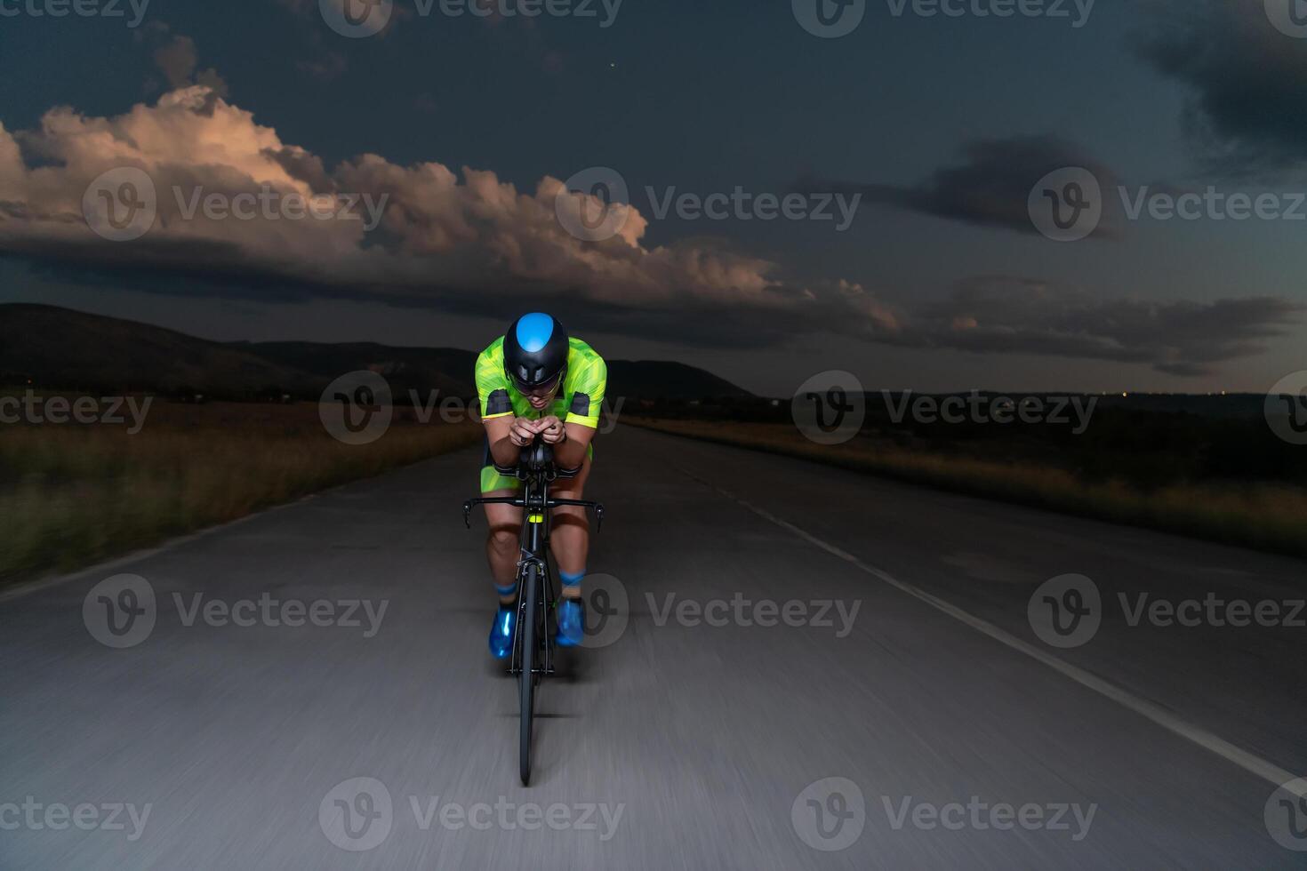 A triathlete rides his bike in the darkness of night, pushing himself to prepare for a marathon. The contrast between the darkness and the light of his bike creates a sense of drama and highlights the photo