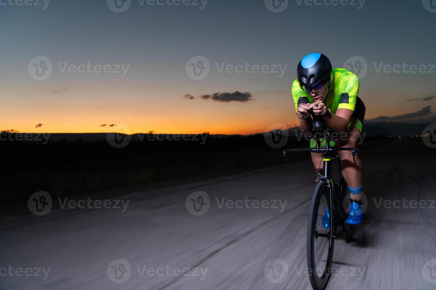 A triathlete rides his bike in the darkness of night, pushing himself to prepare for a marathon. The contrast between the darkness and the light of his bike creates a sense of drama and highlights the photo