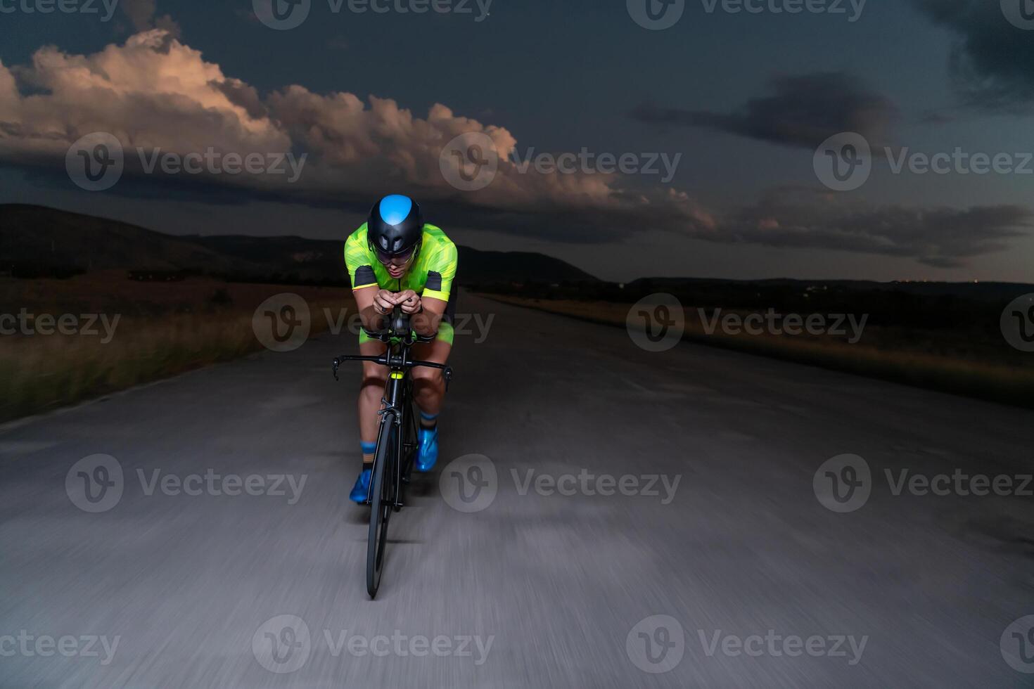 A triathlete rides his bike in the darkness of night, pushing himself to prepare for a marathon. The contrast between the darkness and the light of his bike creates a sense of drama and highlights the photo