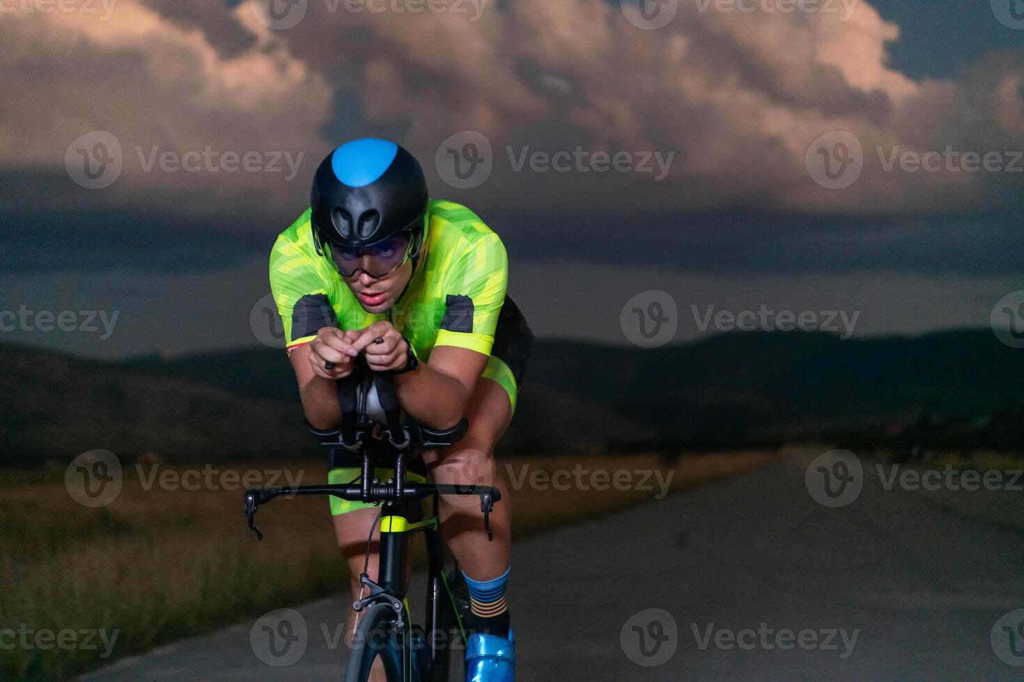 A triathlete rides his bike in the darkness of night, pushing himself to prepare for a marathon. The contrast between the darkness and the light of his bike creates a sense of drama and highlights the photo