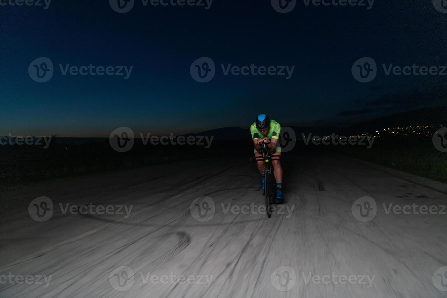 A triathlete rides his bike in the darkness of night, pushing himself to prepare for a marathon. The contrast between the darkness and the light of his bike creates a sense of drama and highlights the photo