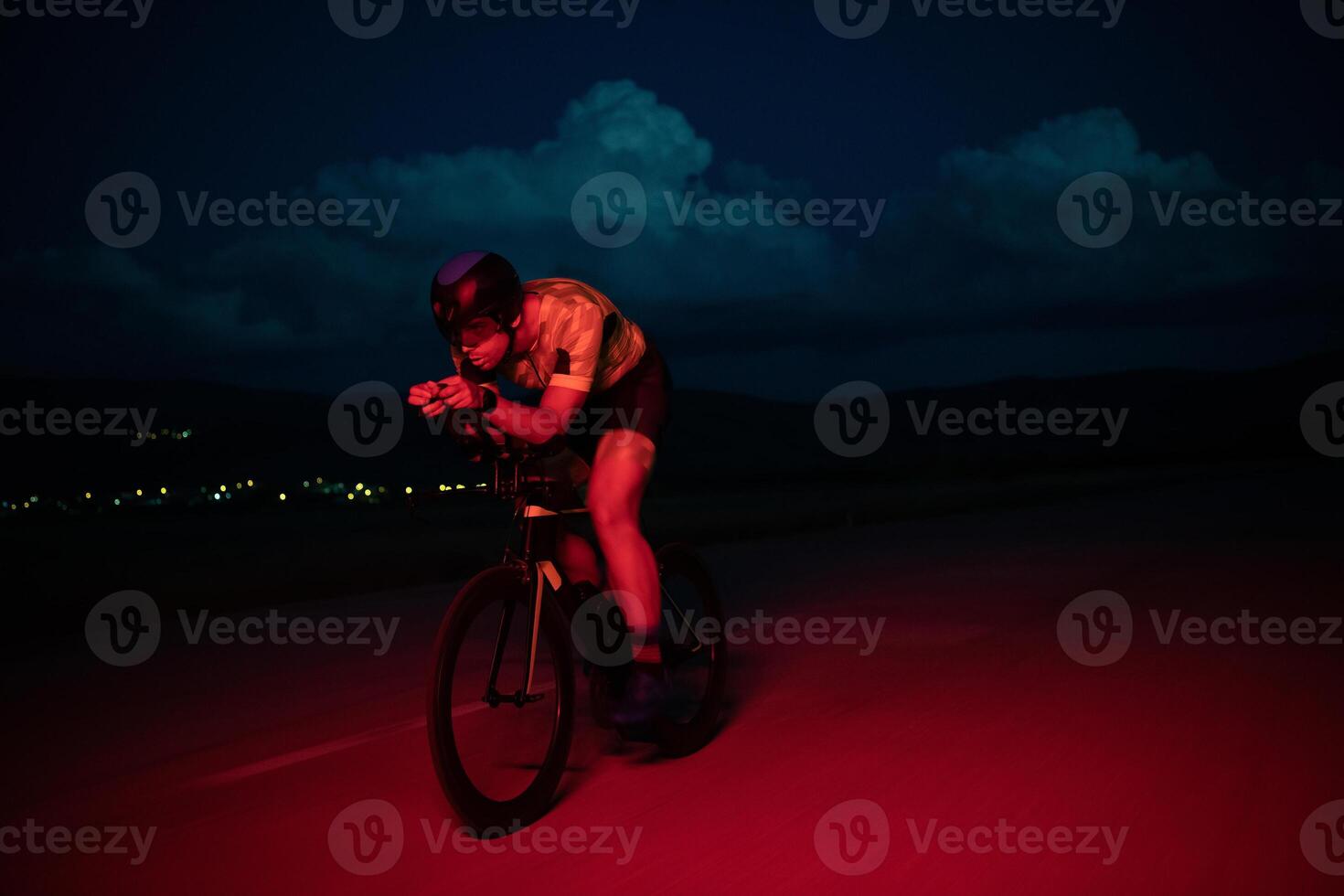 A triathlete rides his bike in the darkness of night, pushing himself to prepare for a marathon. The contrast between the darkness and the light of his bike creates a sense of drama and highlights the photo