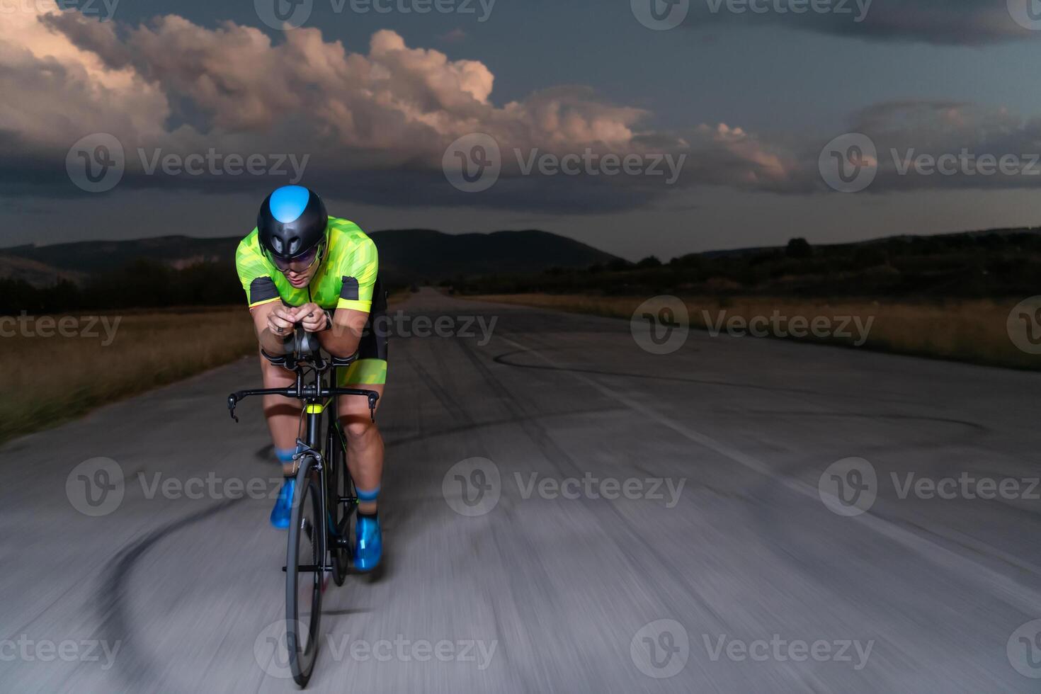 A triathlete rides his bike in the darkness of night, pushing himself to prepare for a marathon. The contrast between the darkness and the light of his bike creates a sense of drama and highlights the photo