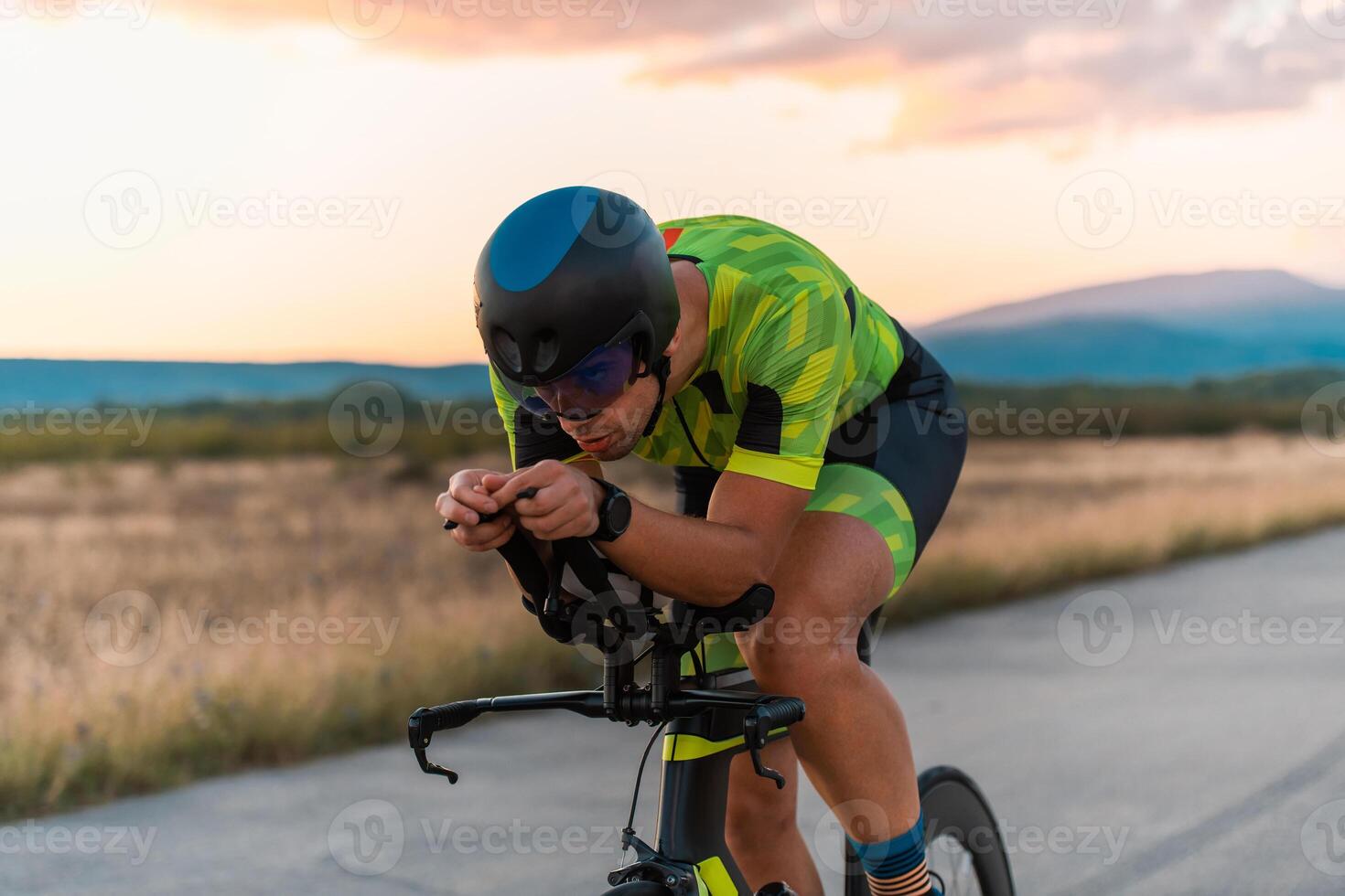 Close up photo of triathlete riding his bicycle during sunset, preparing for a marathon. The warm colors of the sky provide a beautiful backdrop for his determined and focused effort.