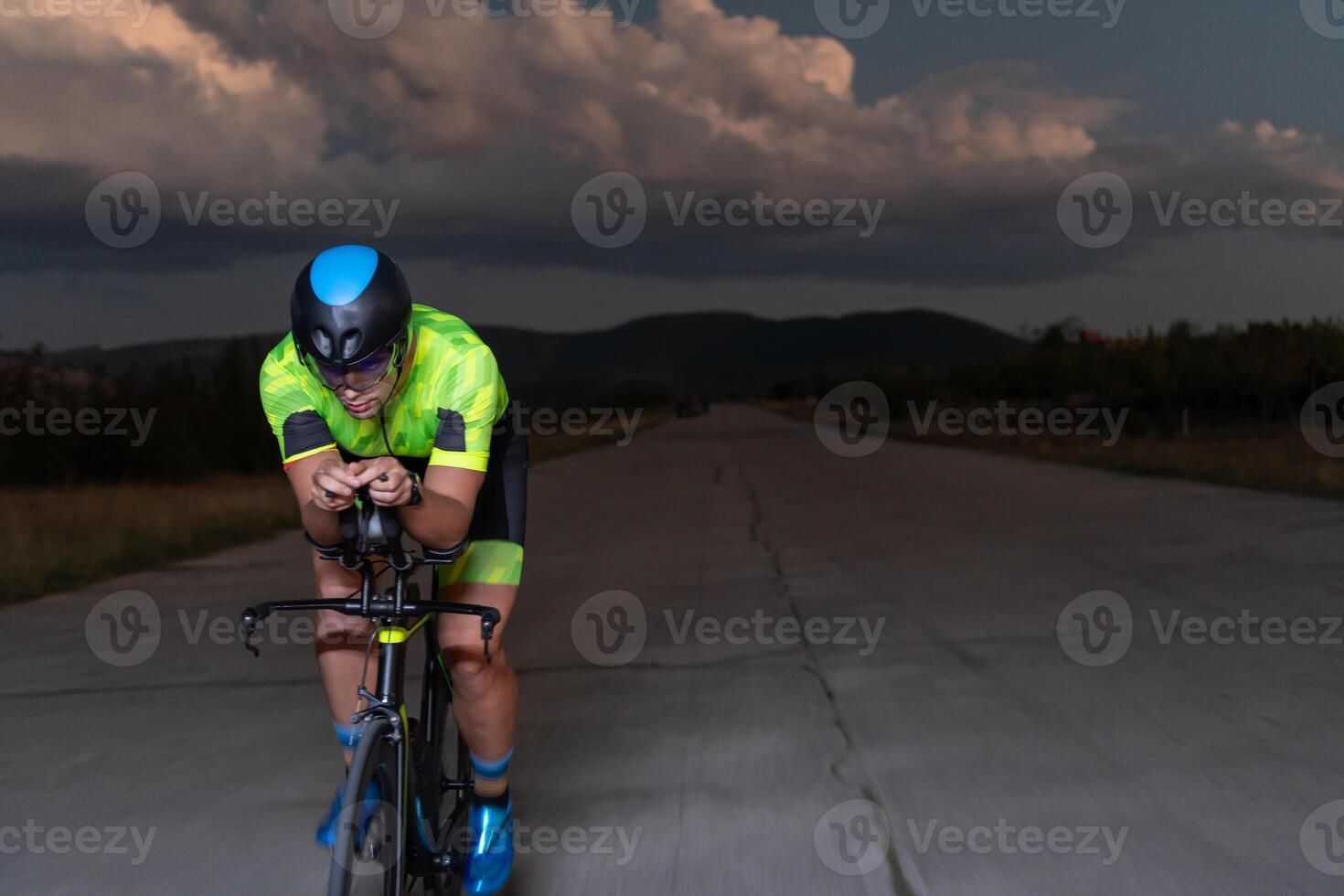 A triathlete rides his bike in the darkness of night, pushing himself to prepare for a marathon. The contrast between the darkness and the light of his bike creates a sense of drama and highlights the photo