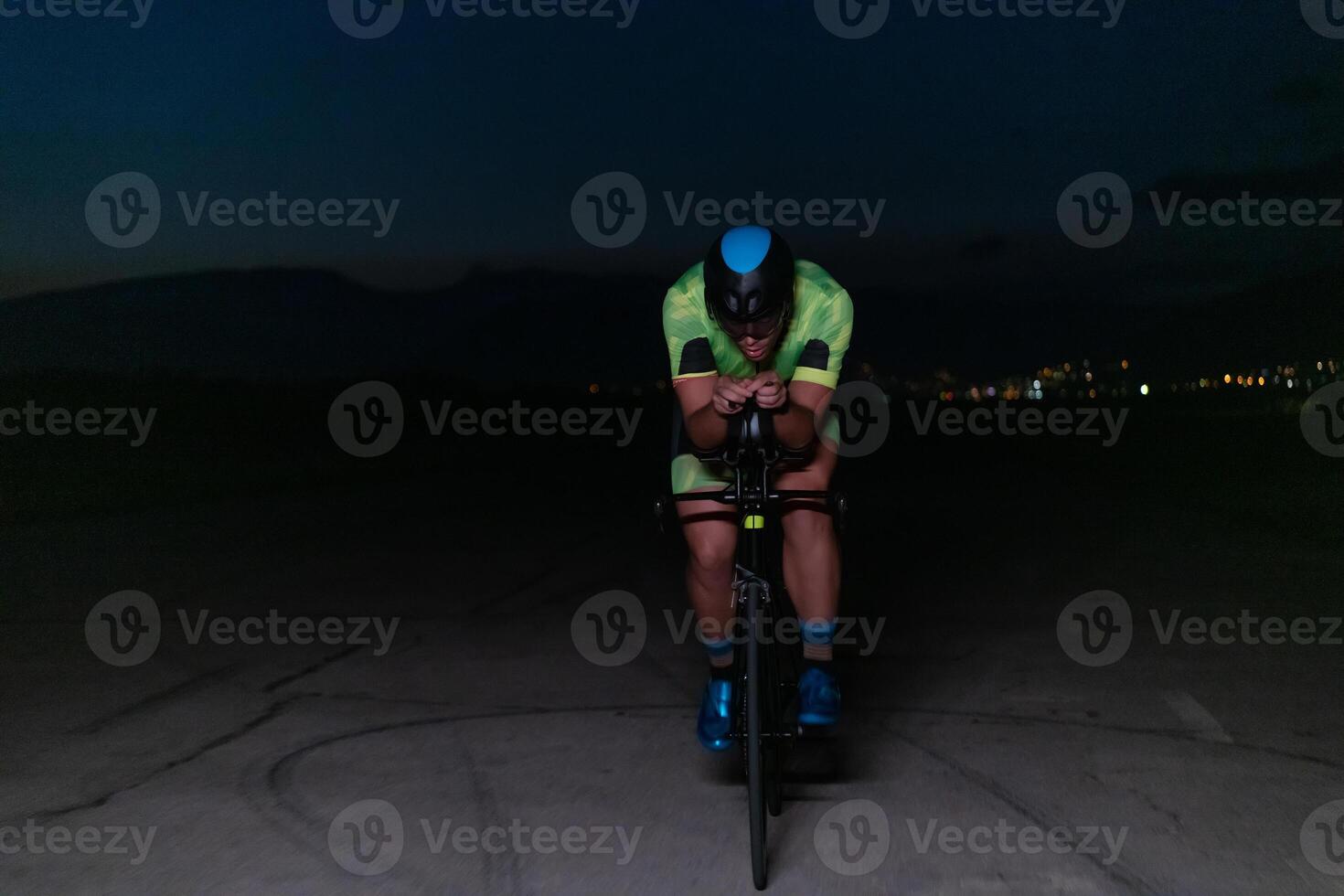 A triathlete rides his bike in the darkness of night, pushing himself to prepare for a marathon. The contrast between the darkness and the light of his bike creates a sense of drama and highlights the photo
