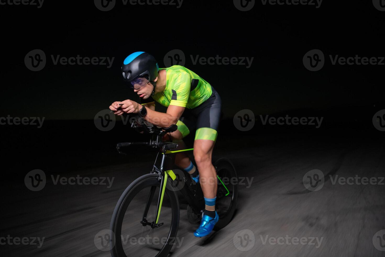 A triathlete rides his bike in the darkness of night, pushing himself to prepare for a marathon. The contrast between the darkness and the light of his bike creates a sense of drama and highlights the photo