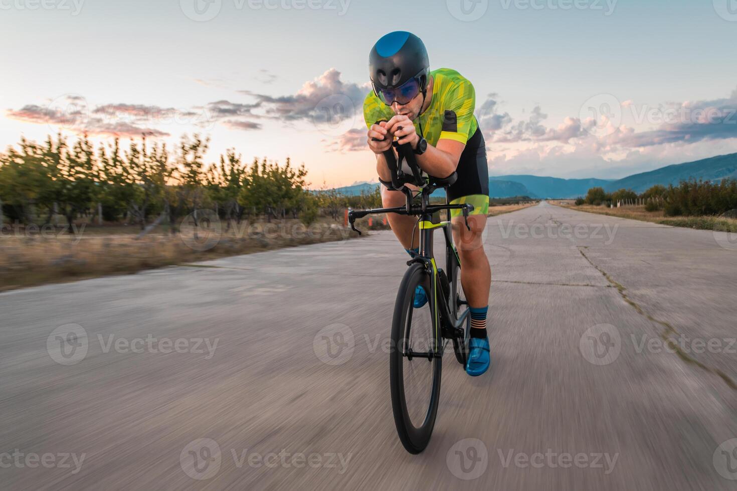 Triathlete riding his bicycle during sunset, preparing for a marathon. The warm colors of the sky provide a beautiful backdrop for his determined and focused effort. photo