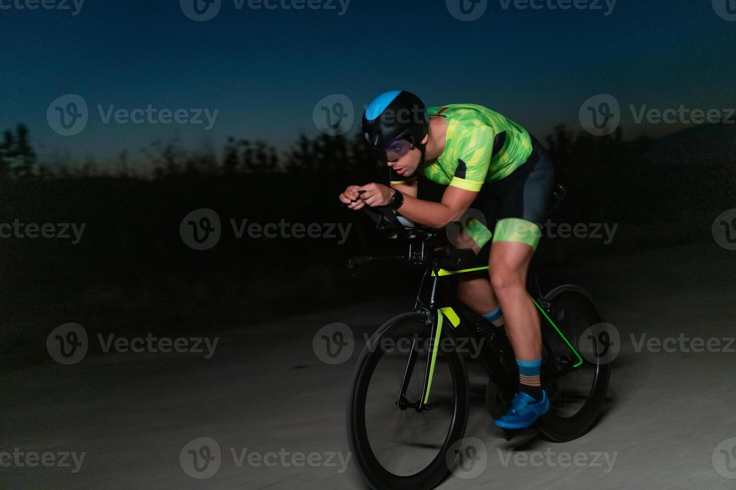 A triathlete rides his bike in the darkness of night, pushing himself to prepare for a marathon. The contrast between the darkness and the light of his bike creates a sense of drama and highlights the photo
