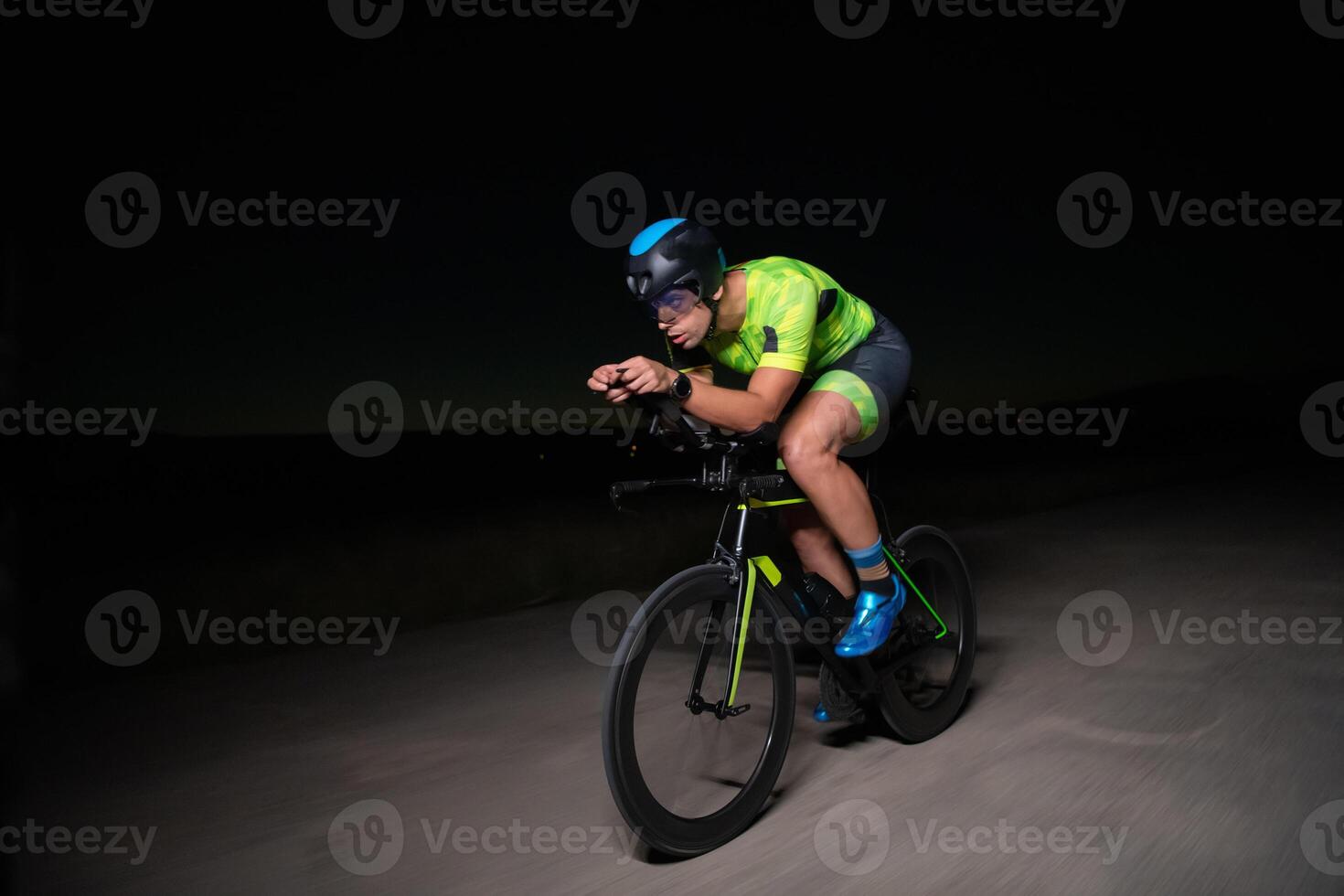 A triathlete rides his bike in the darkness of night, pushing himself to prepare for a marathon. The contrast between the darkness and the light of his bike creates a sense of drama and highlights the photo
