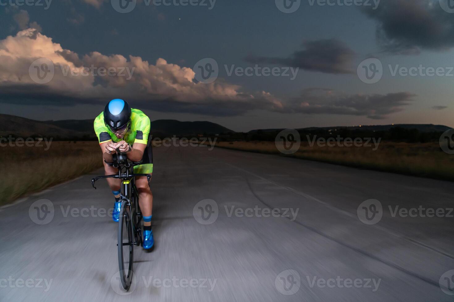 A triathlete rides his bike in the darkness of night, pushing himself to prepare for a marathon. The contrast between the darkness and the light of his bike creates a sense of drama and highlights the photo