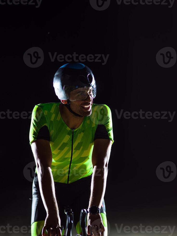 A triathlete rides his bike in the darkness of night, pushing himself to prepare for a marathon. The contrast between the darkness and the light of his bike creates a sense of drama and highlights the photo