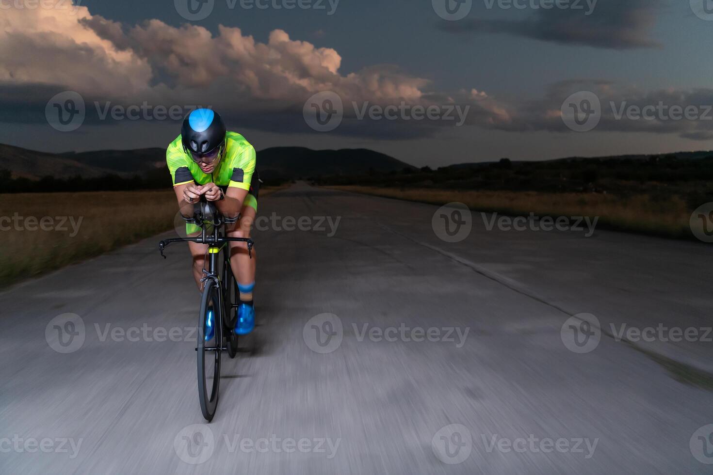 A triathlete rides his bike in the darkness of night, pushing himself to prepare for a marathon. The contrast between the darkness and the light of his bike creates a sense of drama and highlights the photo