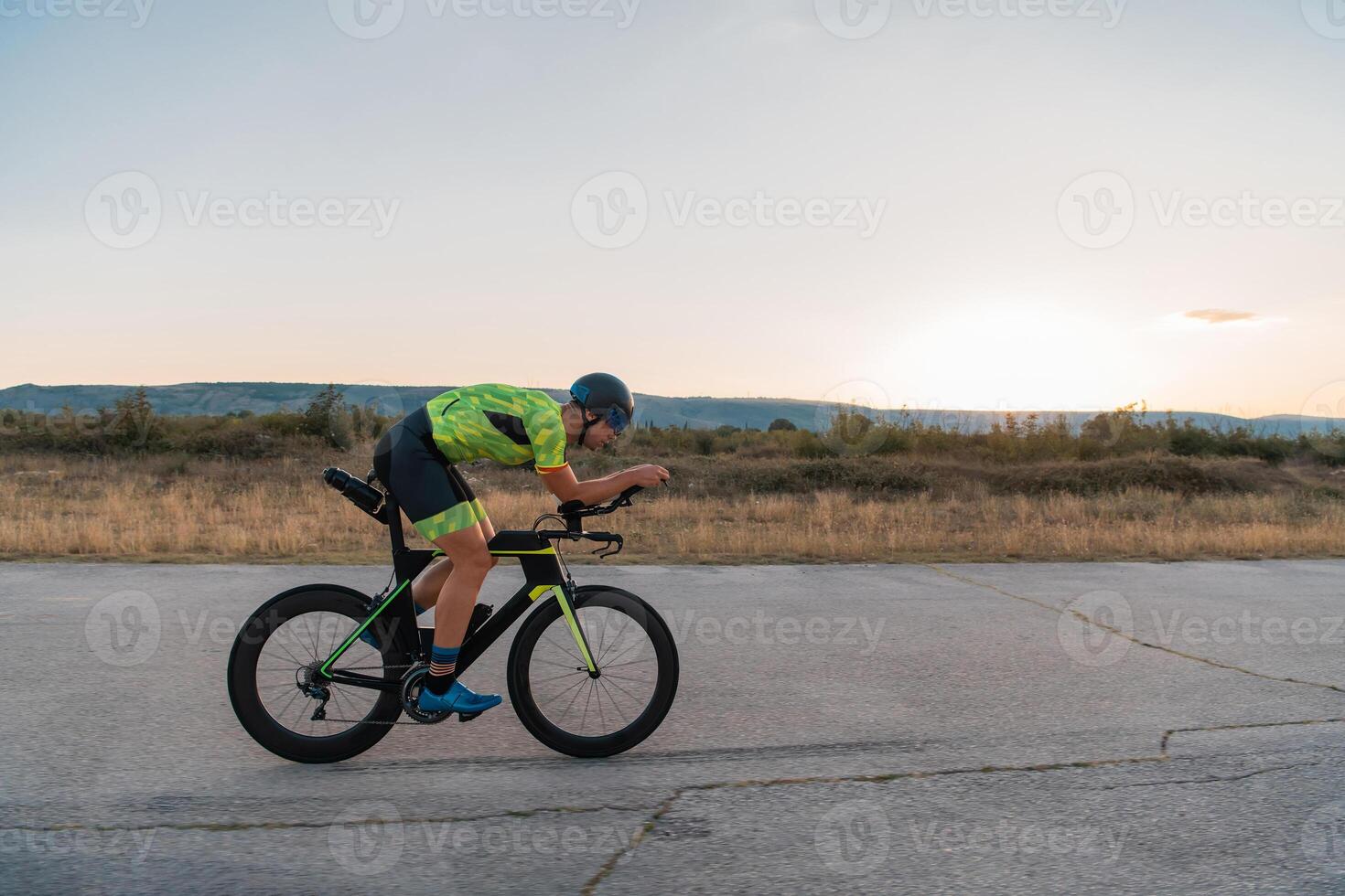 Triathlete riding his bicycle during sunset, preparing for a marathon. The warm colors of the sky provide a beautiful backdrop for his determined and focused effort. photo