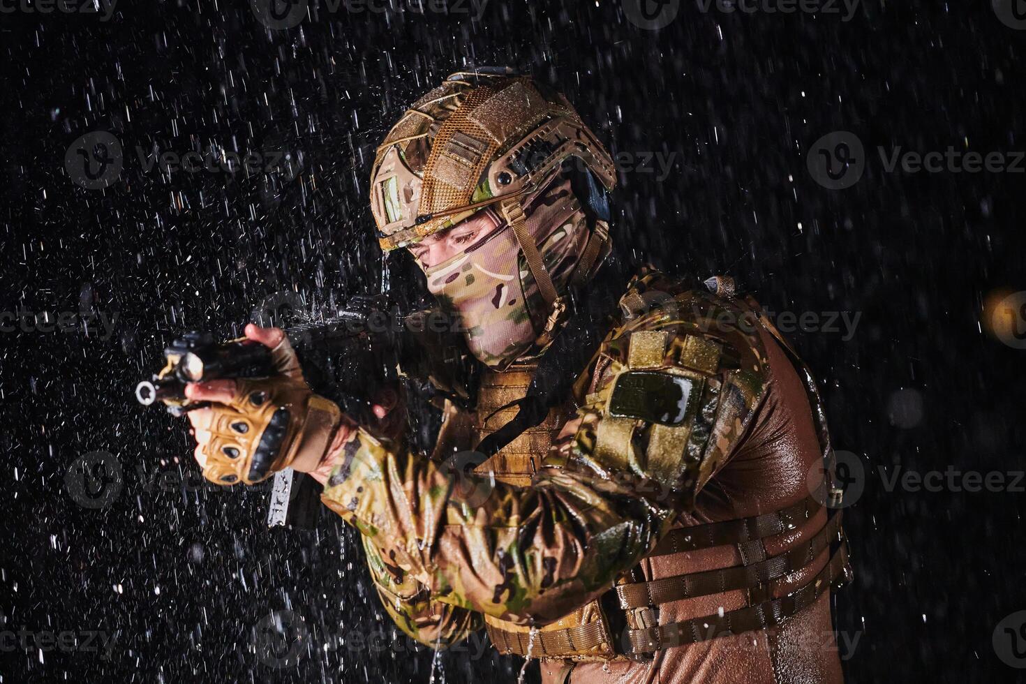 Army soldier in Combat Uniforms with an assault rifle, plate carrier and combat helmet going on a dangerous mission on a rainy night. photo
