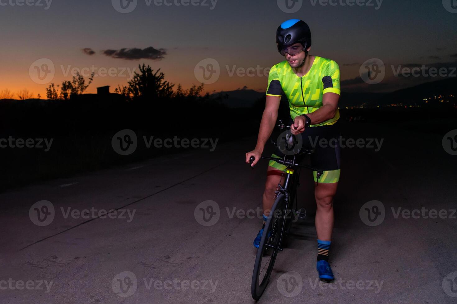 A triathlete rides his bike in the darkness of night, pushing himself to prepare for a marathon. The contrast between the darkness and the light of his bike creates a sense of drama and highlights the photo