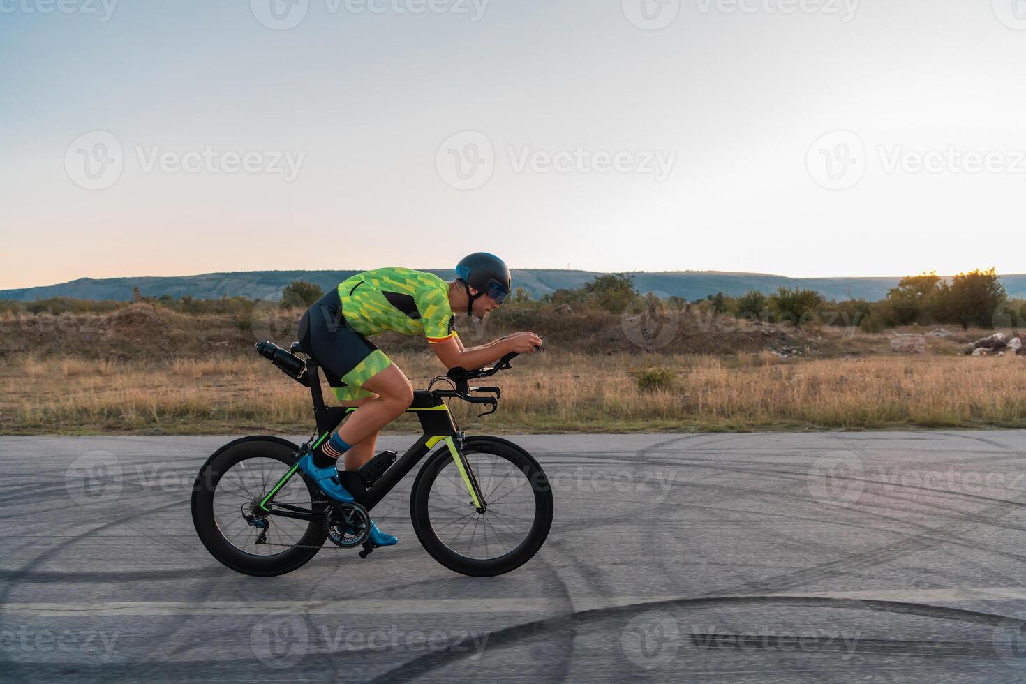 Triathlete riding his bicycle during sunset, preparing for a marathon. The warm colors of the sky provide a beautiful backdrop for his determined and focused effort. photo