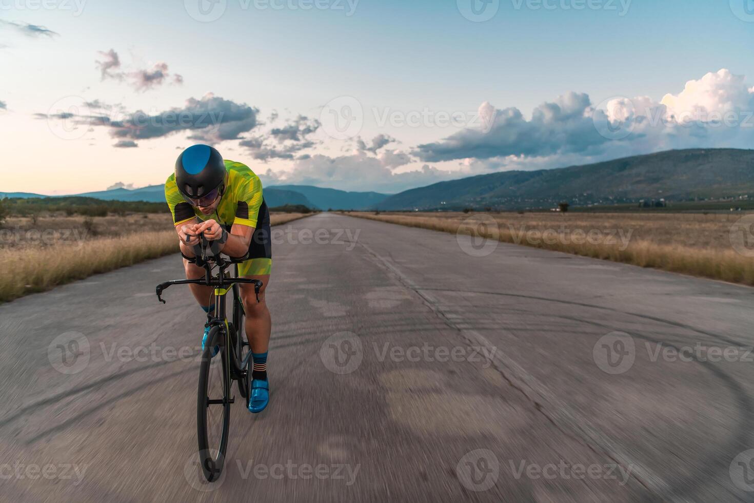 Triathlete riding his bicycle during sunset, preparing for a marathon. The warm colors of the sky provide a beautiful backdrop for his determined and focused effort. photo