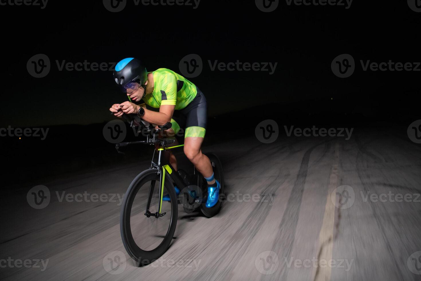 A triathlete rides his bike in the darkness of night, pushing himself to prepare for a marathon. The contrast between the darkness and the light of his bike creates a sense of drama and highlights the photo