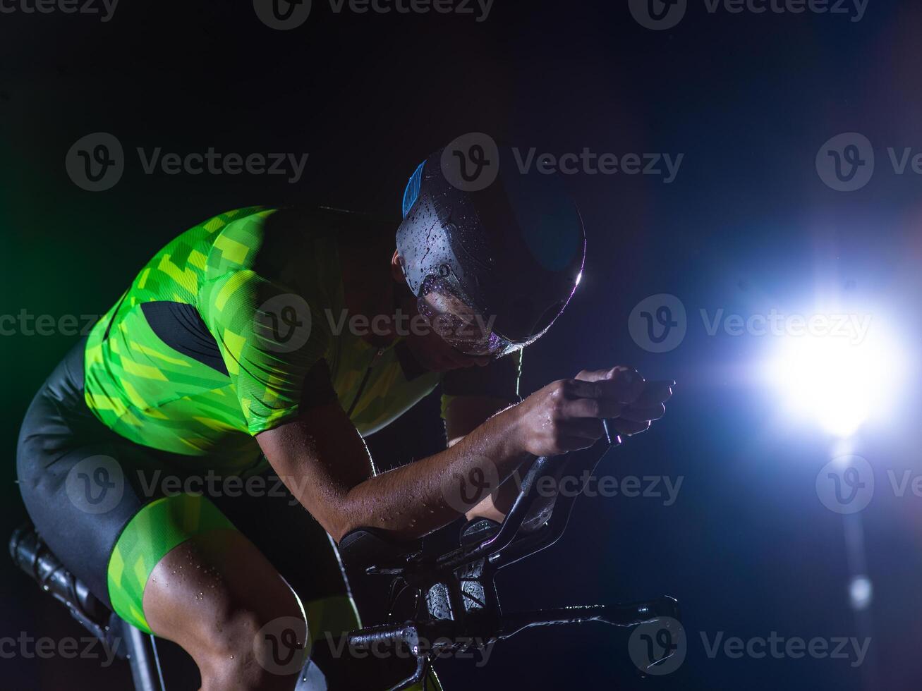 A triathlete rides his bike in the darkness of night, pushing himself to prepare for a marathon. The contrast between the darkness and the light of his bike creates a sense of drama and highlights the photo