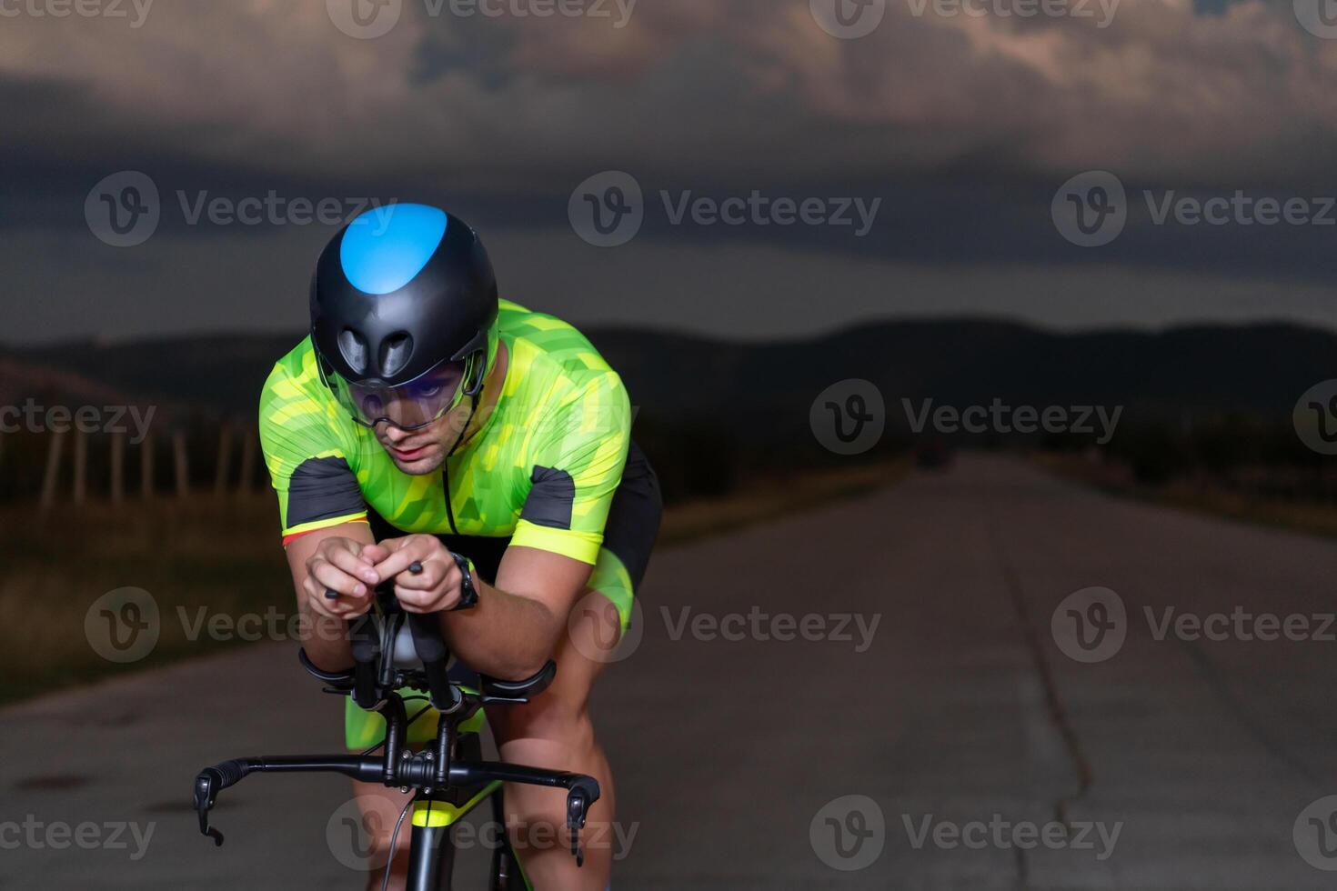 A triathlete rides his bike in the darkness of night, pushing himself to prepare for a marathon. The contrast between the darkness and the light of his bike creates a sense of drama and highlights the photo