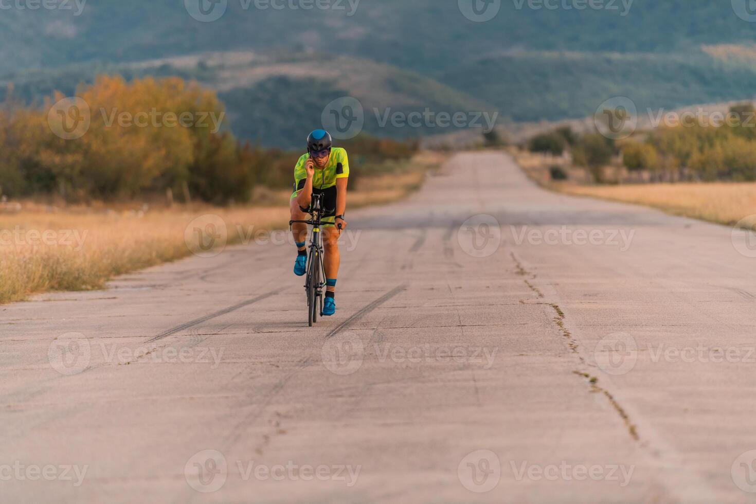 Triathlete riding his bicycle during sunset, preparing for a marathon. The warm colors of the sky provide a beautiful backdrop for his determined and focused effort. photo