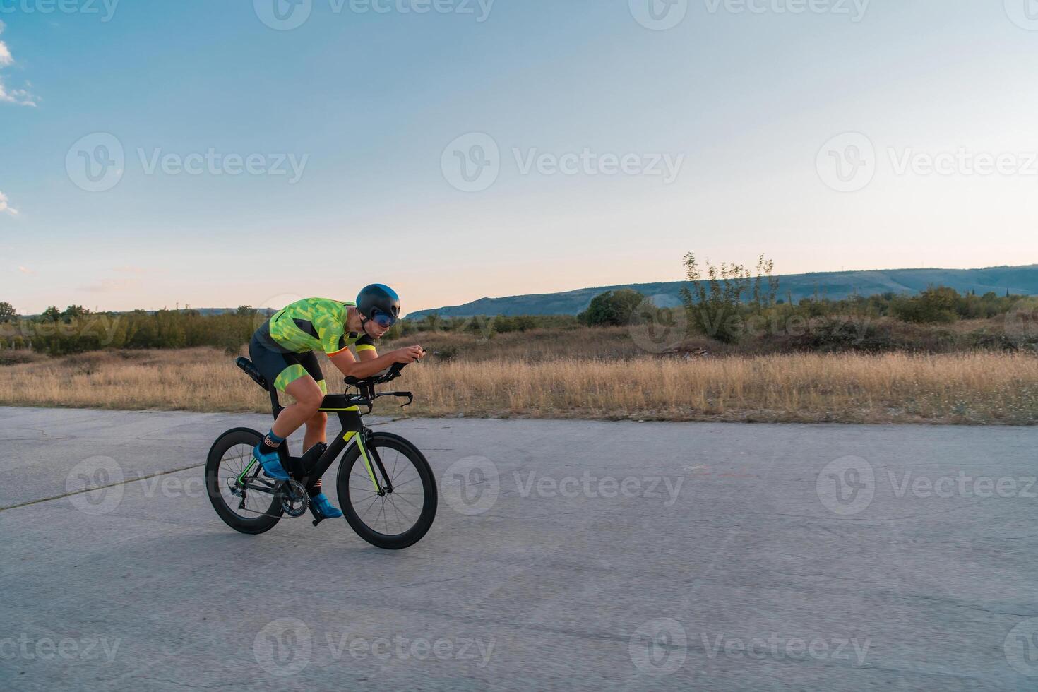 Triathlete riding his bicycle during sunset, preparing for a marathon. The warm colors of the sky provide a beautiful backdrop for his determined and focused effort. photo