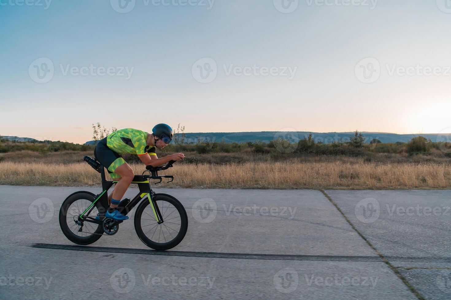 Triathlete riding his bicycle during sunset, preparing for a marathon. The warm colors of the sky provide a beautiful backdrop for his determined and focused effort. photo