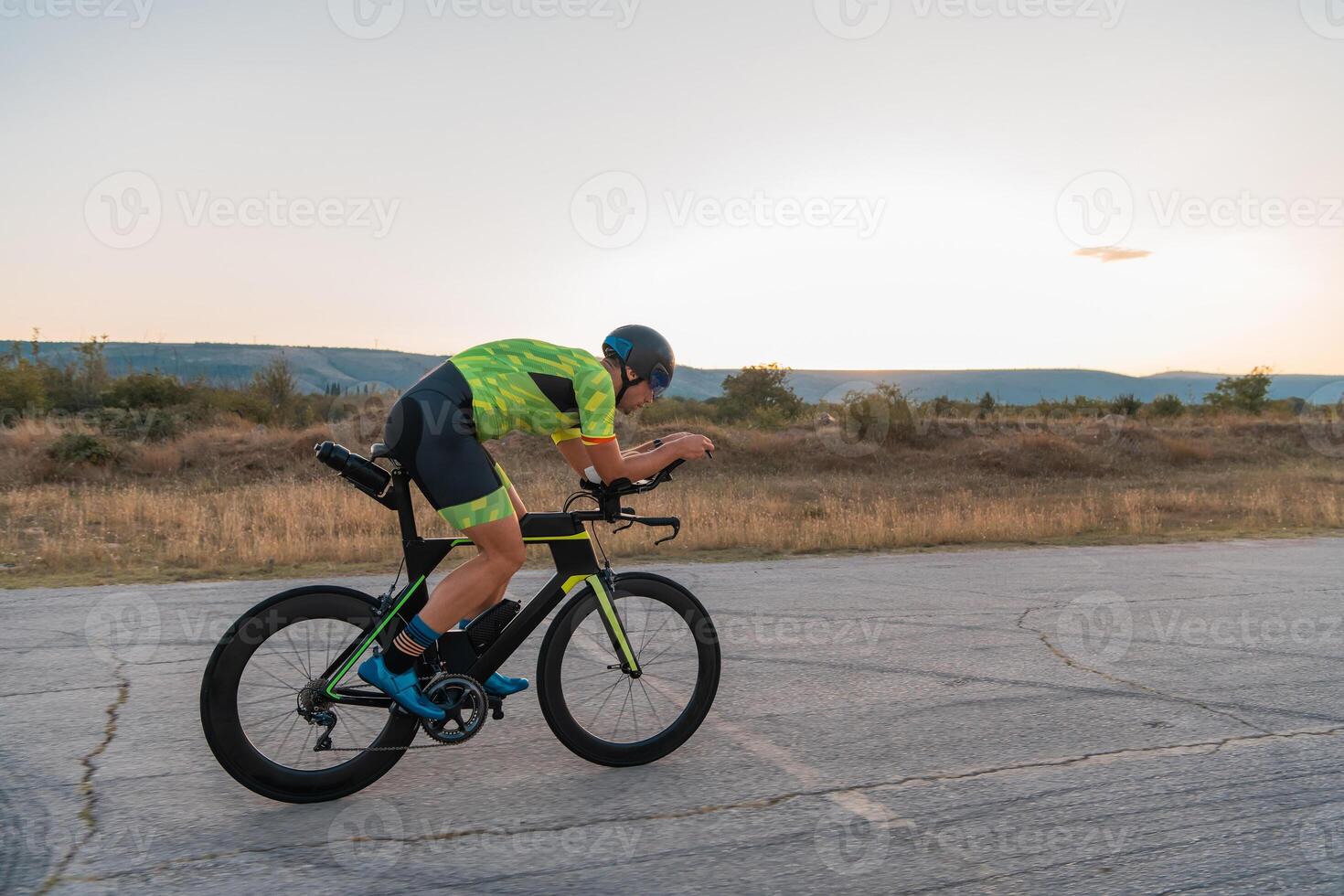 Triathlete riding his bicycle during sunset, preparing for a marathon. The warm colors of the sky provide a beautiful backdrop for his determined and focused effort. photo