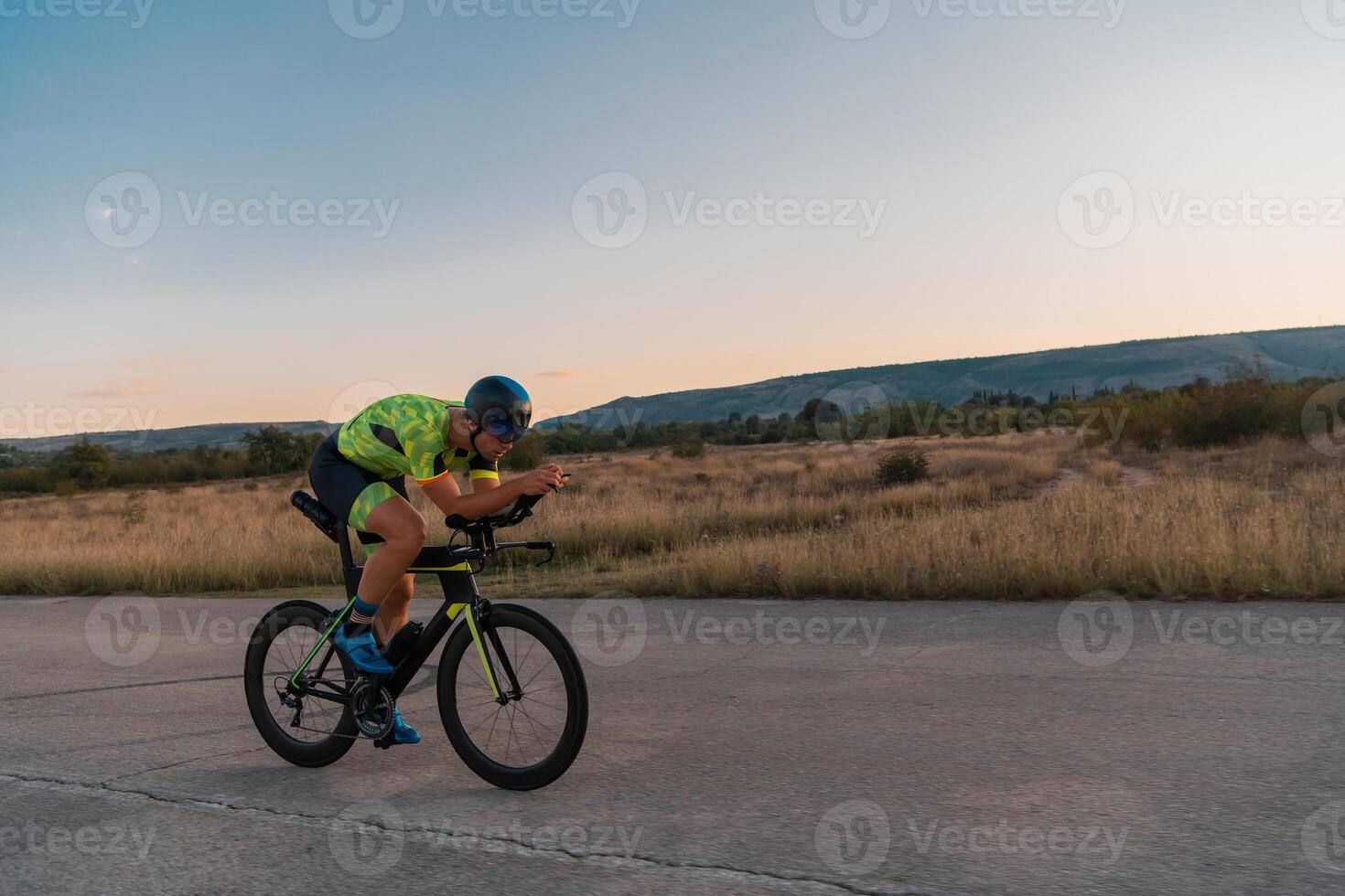 Triathlete riding his bicycle during sunset, preparing for a marathon. The warm colors of the sky provide a beautiful backdrop for his determined and focused effort. photo