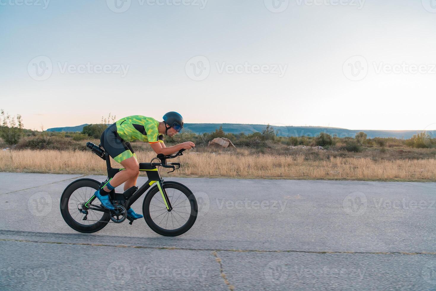 Triathlete riding his bicycle during sunset, preparing for a marathon. The warm colors of the sky provide a beautiful backdrop for his determined and focused effort. photo