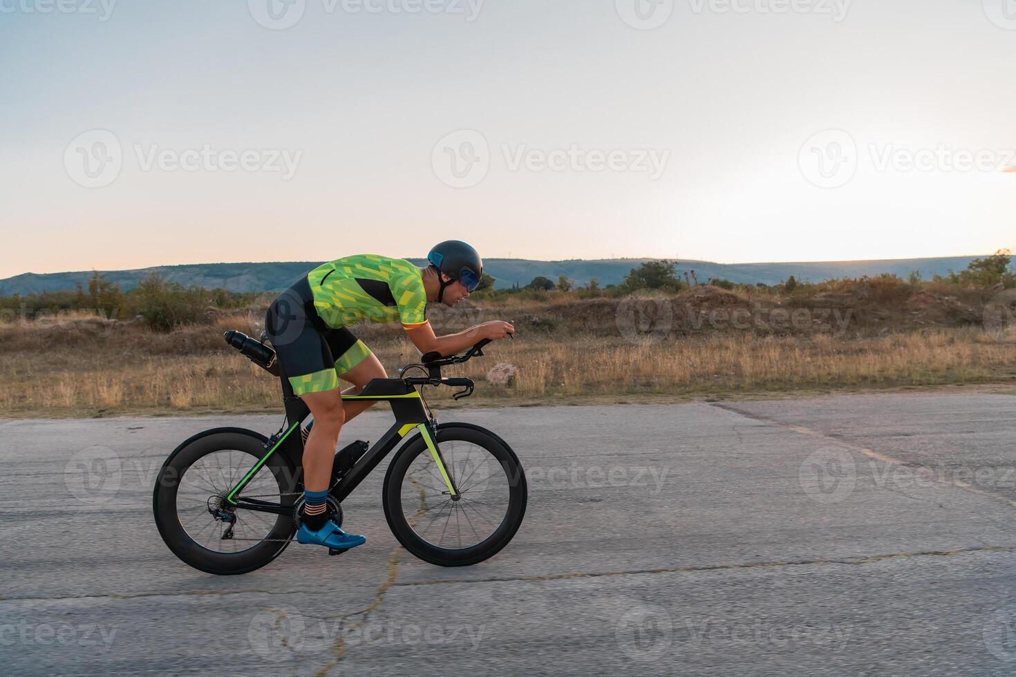 Triathlete riding his bicycle during sunset, preparing for a marathon. The warm colors of the sky provide a beautiful backdrop for his determined and focused effort. photo
