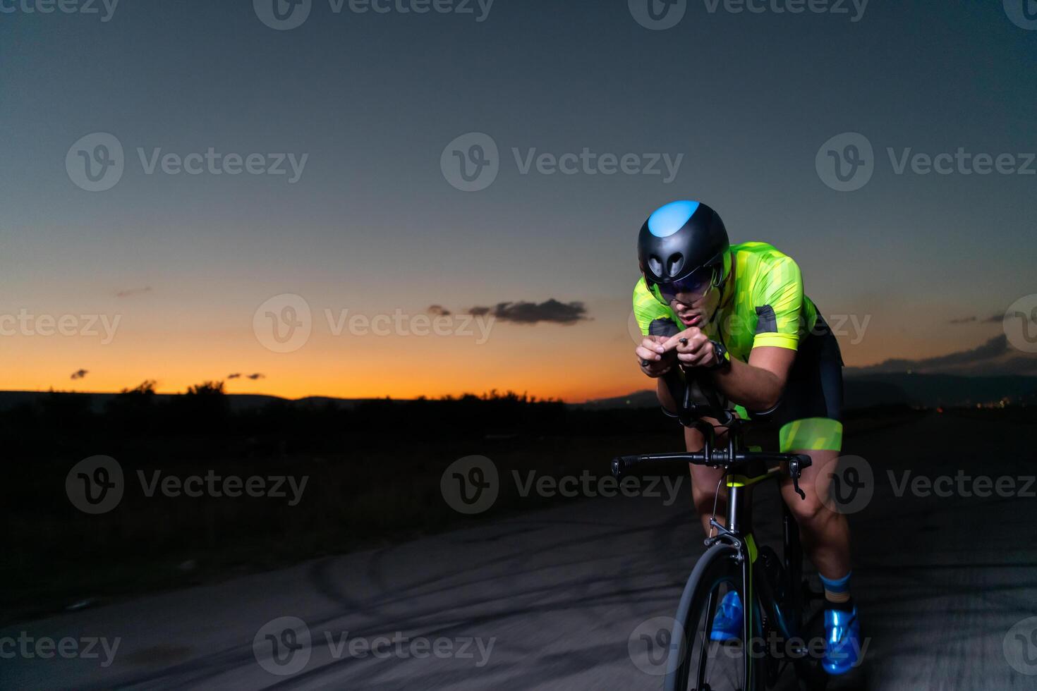 A triathlete rides his bike in the darkness of night, pushing himself to prepare for a marathon. The contrast between the darkness and the light of his bike creates a sense of drama and highlights the photo