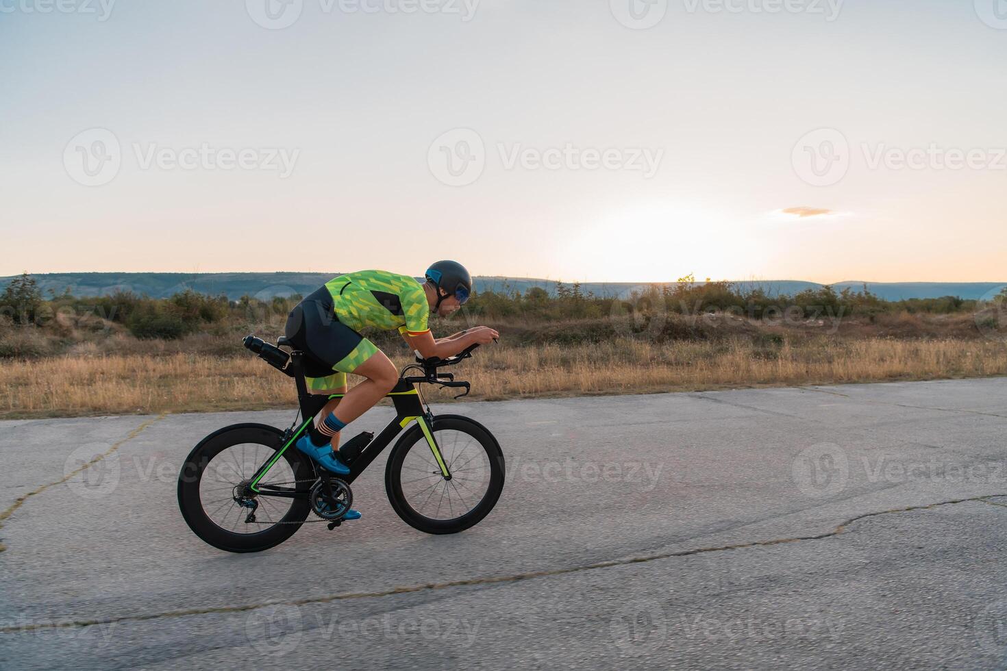 Triathlete riding his bicycle during sunset, preparing for a marathon. The warm colors of the sky provide a beautiful backdrop for his determined and focused effort. photo