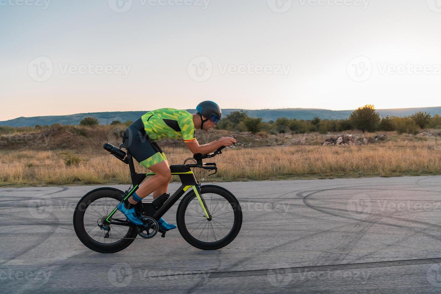 Triathlete riding his bicycle during sunset, preparing for a marathon. The warm colors of the sky provide a beautiful backdrop for his determined and focused effort. photo