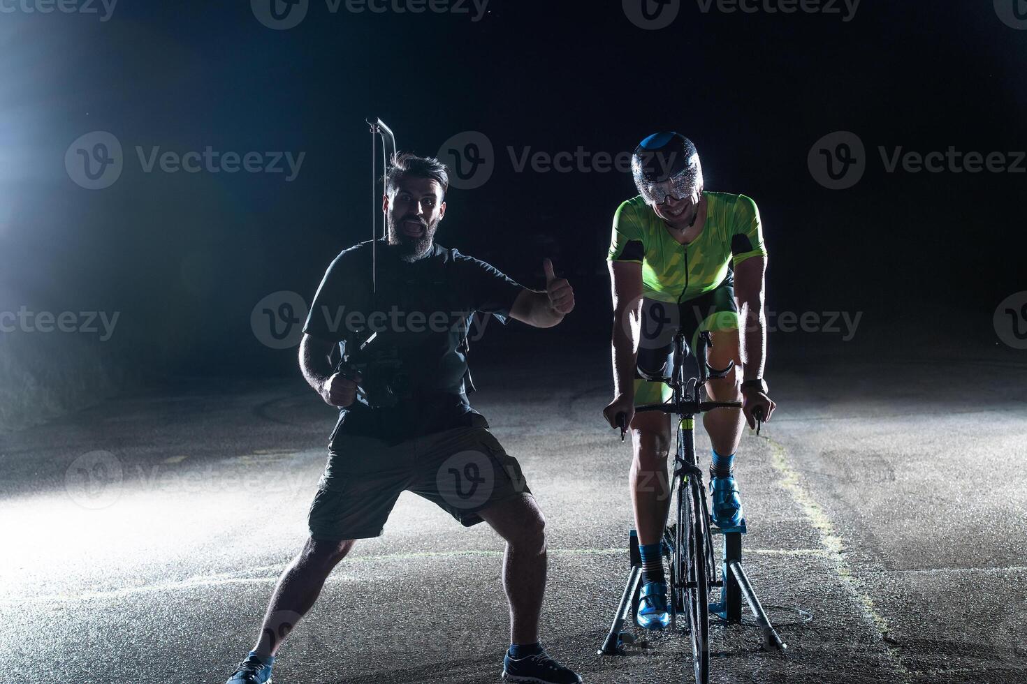 Behind the scenes. Professional videographer on a night shoot with a triathlete riding a bicycle for recording purposes photo