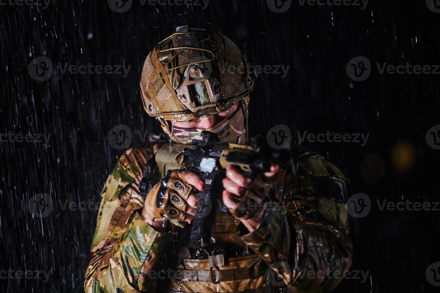 Army soldier in Combat Uniforms with an assault rifle, plate carrier and combat helmet going on a dangerous mission on a rainy night. photo